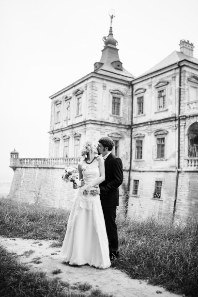 爱的新婚夫妇在他们幸福的婚礼日背景古老的城堡在多云的天气。黑白照片图片下载