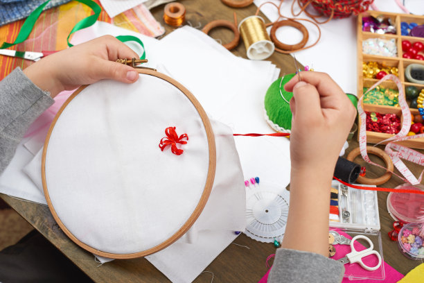 男孩在箍上刺绣，手的特写和红色丝带在白色纺织品上，学习缝纫，职业培训，手工和手工艺概念图片下载