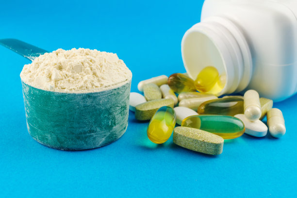蛋白质粉在测量塑料匙和维生素复合，欧米茄3，葡萄糖胺胶囊，补充蓝色背景，运动营养素材图片