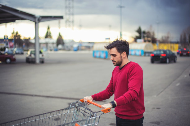 一个年轻人在超市附近的停车场推着购物车图片下载