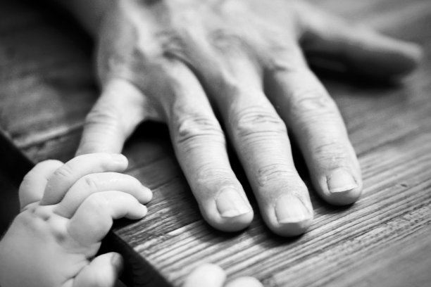 婴儿伸手去抓放在木桌上的爷爷的手图片下载