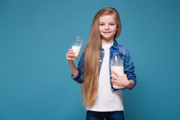 穿着牛仔夹克，棕色长发的漂亮小女孩拿着牛奶盒图片下载