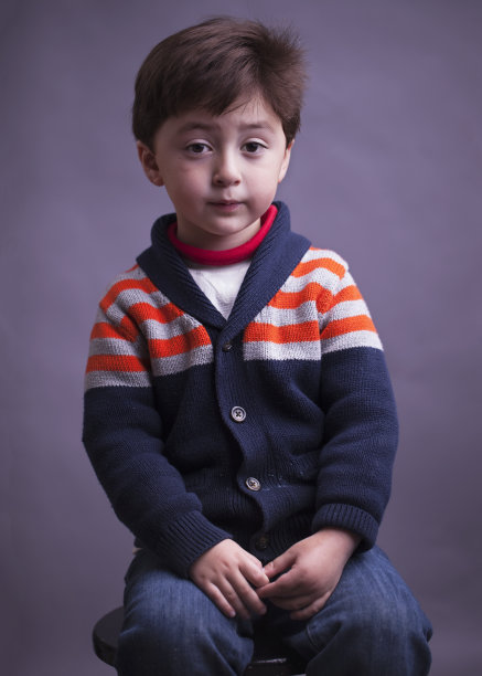 这是一幅悲伤严肃的多种族白人小男孩的肖像，他的头发是棕色，穿着一件带橙色条纹的蓝色针织毛衣图片下载