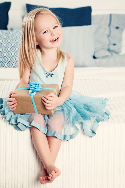 笑着的小女孩在家里拿着礼物。孩子与生日礼盒素材图片