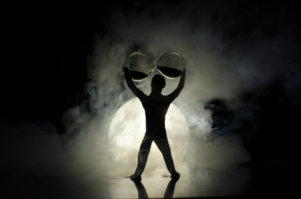 概念图像与沙漏和和人与月亮在背景与雾。触摸沙漏的玩具人物剪影。最后期限的概念。图片下载