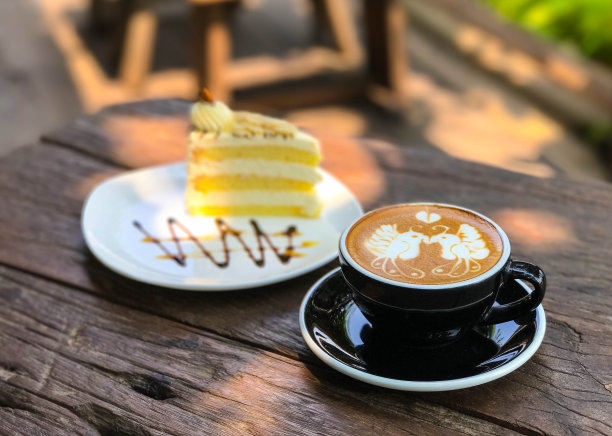 拿铁艺术咖啡设计约2鸟和心形的黑色杯在旧木书桌上与蛋糕的背景图片下载