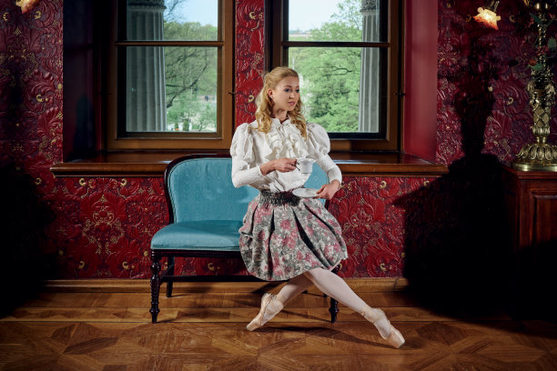 年轻的金发芭蕾舞女穿着时尚的衣服坐在沙发上喝茶图片下载