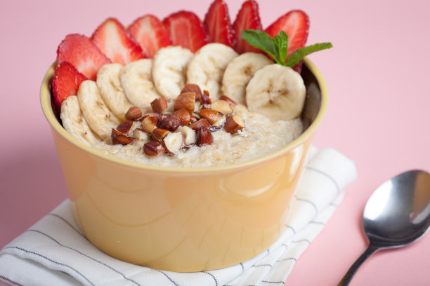 一碗有香蕉、草莓、杏仁、榛子和奶油的粉色燕麦粥。热腾腾的健康早餐，俯视图素材图片