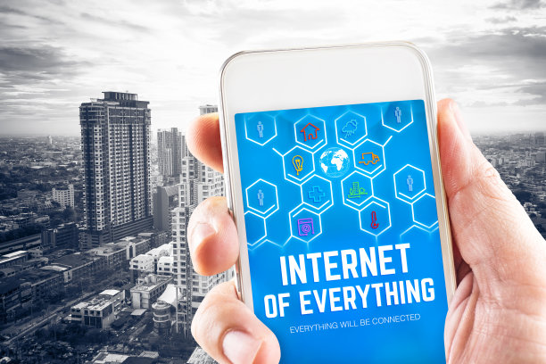 近距离手持手机，屏幕上显示万物互联(IOE)字，黑白城市景观背景，数字智能技术理念图片下载