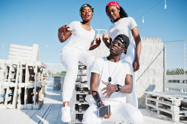 三个时髦的非裔美国朋友，穿着白色衣服在海滩的码头上。年轻黑人的街头时尚。一个黑人和两个非洲女孩。图片下载