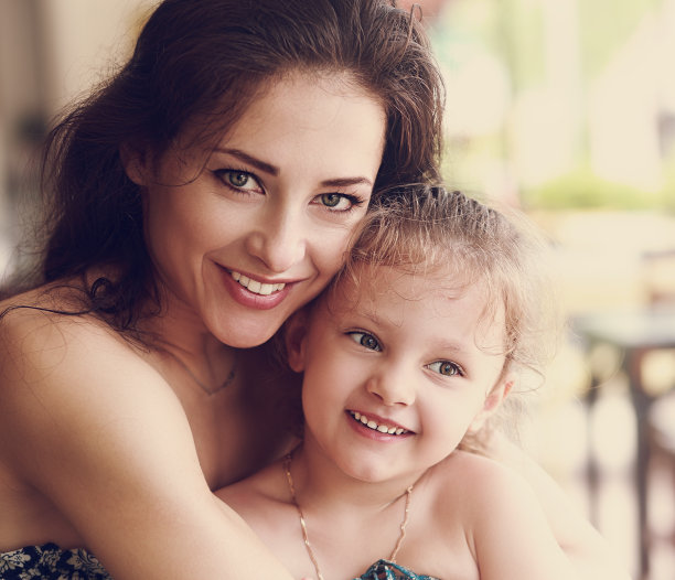 幸福美丽的母亲拥抱她的女儿微笑在咖啡馆。图片下载