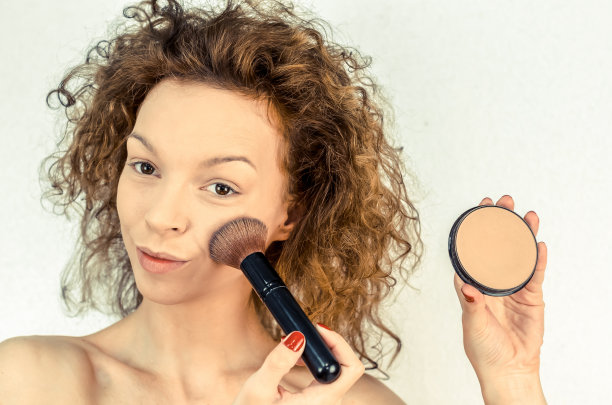 美丽的卷发女孩在脸颊上敷了一个粉饼图片下载