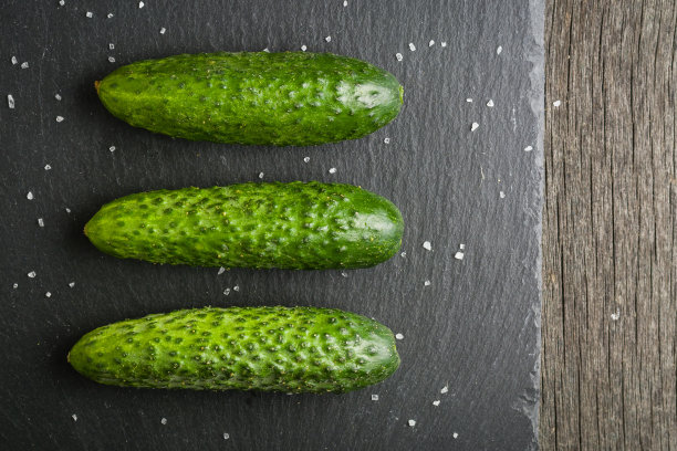 几根新鲜的绿黄瓜并排躺在一块黑色的石头上。一个简约的照片。图片下载