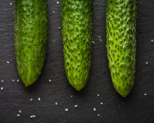 几根新鲜的绿黄瓜并排躺在一块黑色的石头上。一个简约的照片。图片下载