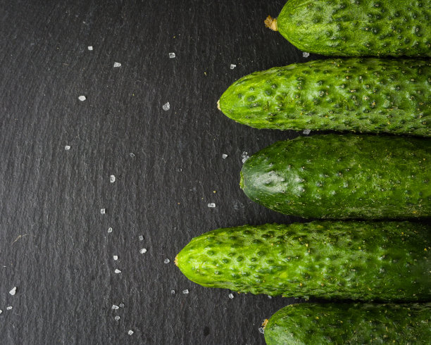 几根新鲜的绿黄瓜并排躺在一块黑色的石头上。一个简约的照片。图片下载