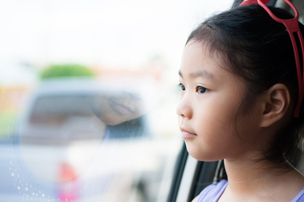 小女孩坐在车里透过窗户往外看。图片下载