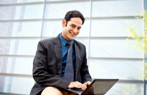 聪明的印度商人在办公大楼前使用笔记本电脑图片下载