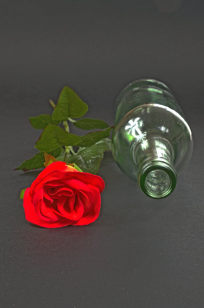 黑色背景上的红玫瑰和空瓶子图片下载