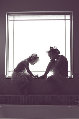 一个小女孩给一个带卷发器的女孩涂指甲油图片下载