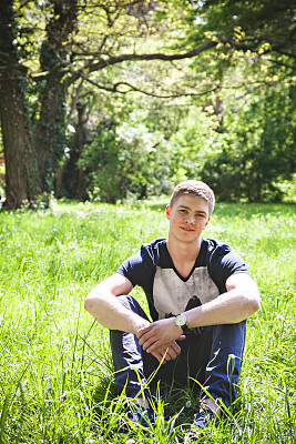 年轻人坐在公园的草地上图片下载