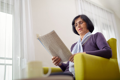 老年妇女一边在家休息一边看报纸图片下载