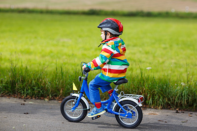 可爱的小男孩戴着头盔，穿着五颜六色的外套骑着自行车图片下载