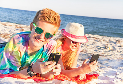 青少年在海滩上使用智能手机和听音乐。图片下载