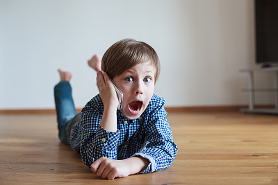 男孩躺在木地板上打电话图片下载