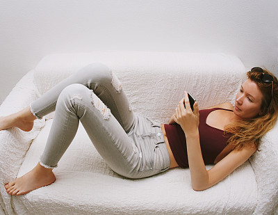 女孩拿着手机，躺在沙发上。图片下载