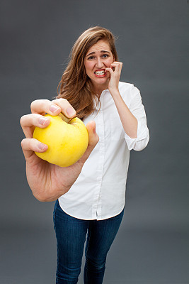 紧张的年轻美丽的女人咬紧牙关拿着一个苹果图片下载
