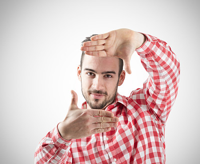 年轻的胡子男子展示手指框架看着相机图片下载