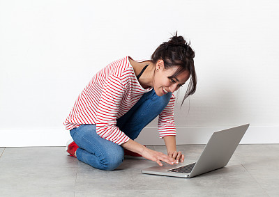 微笑的漂亮女孩坐在地板上，在电脑上工作图片下载