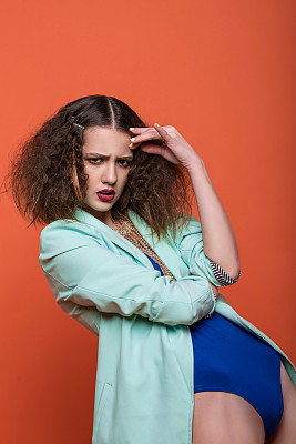 时尚照片的美丽女孩在工作室。年轻的黑发女子在蓝色内衣和绿松石夹克摆姿势在红色的背景。卷曲的发型。图片下载