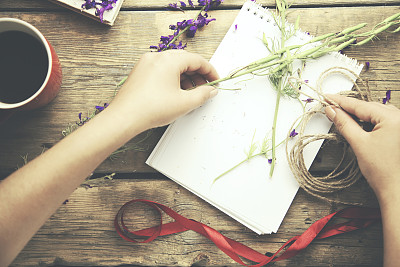 女人手拿缎带、鲜花、笔记本和咖啡放在桌上图片下载