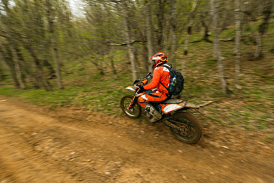男人骑着鲜艳的橙色摩托车在森林里飞驰。运动中的模糊背景图片下载