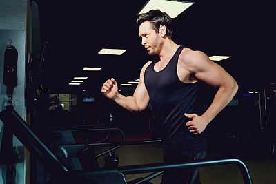 一名男子运动员在黑暗的健身房跑步机上慢跑图片下载