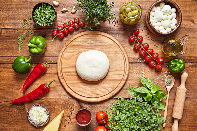 意大利菜的烹饪背景。比萨烹饪配料:生面团，马苏里拉奶酪，西红柿，罗勒，橄榄油，奶酪，酱汁，瑞加诺，帕尔马干酪，胡椒，香草放在质朴的木桌上。图片下载