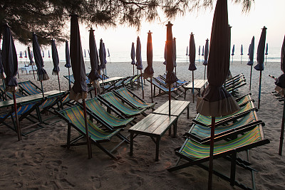 在海边日出时，在一个荒芜的海滩上折叠沙滩伞。低的季节。空的日光浴浴床。图片下载