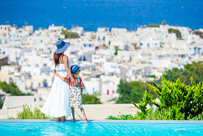 可爱的小女孩和年轻的母亲在室外游泳池背景米科诺斯镇，基克拉迪斯，希腊图片下载