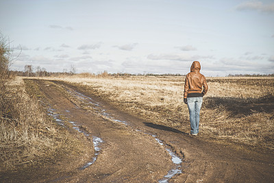 女孩走在泥泞的乡间小路上。早春的时间。复古风格。图片下载