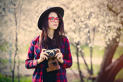 美丽的年轻女子与相机站在美丽的盛开的树木前面图片下载