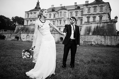 爱的新婚夫妇在他们幸福的婚礼日背景古老的城堡在多云的天气。黑白照片图片下载