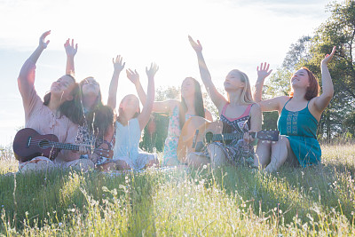 女孩们一起坐在草地上，高举双臂，唱着歌，演奏着乐器图片下载