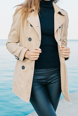 穿着米色外套和黑色裤子的苗条女孩在海滩上图片下载