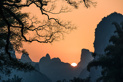 夕阳在以树干为前景的山峦中，聚焦于树木图片下载