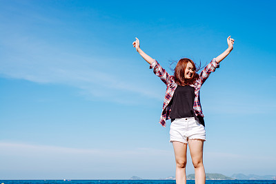 女人放松在海滩享受夏天的自由与开放的手臂和头发在水海边的风。亚洲女孩在夏季旅游假期假期外。复古效果风格的图片。图片下载