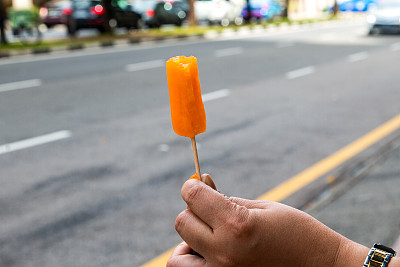 在道路背景中，一只手拿着橙色的冰淇淋图片下载