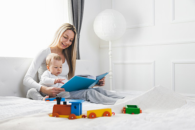 孩子的教育。快乐的妈妈和她的孩子坐在床上看书图片下载