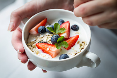 女人手里拿着碗，里面有美味的水果，燕麦和酸奶。特写镜头。健康食品的概念。图片下载
