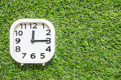 特写白色时钟装饰显示12点15分或下午12点15分在绿色人造草地板纹理背景与复制空间图片下载